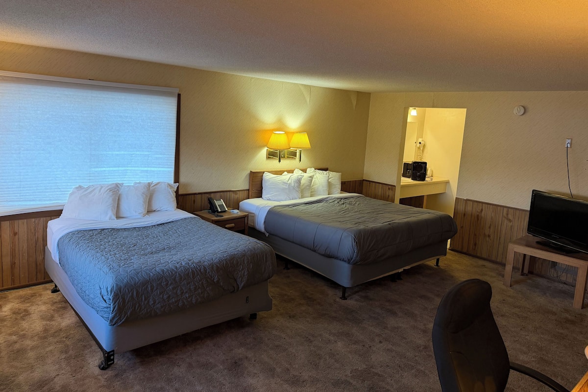 A hotel room with two beds, a desk, a chair, a television, and a large window.
