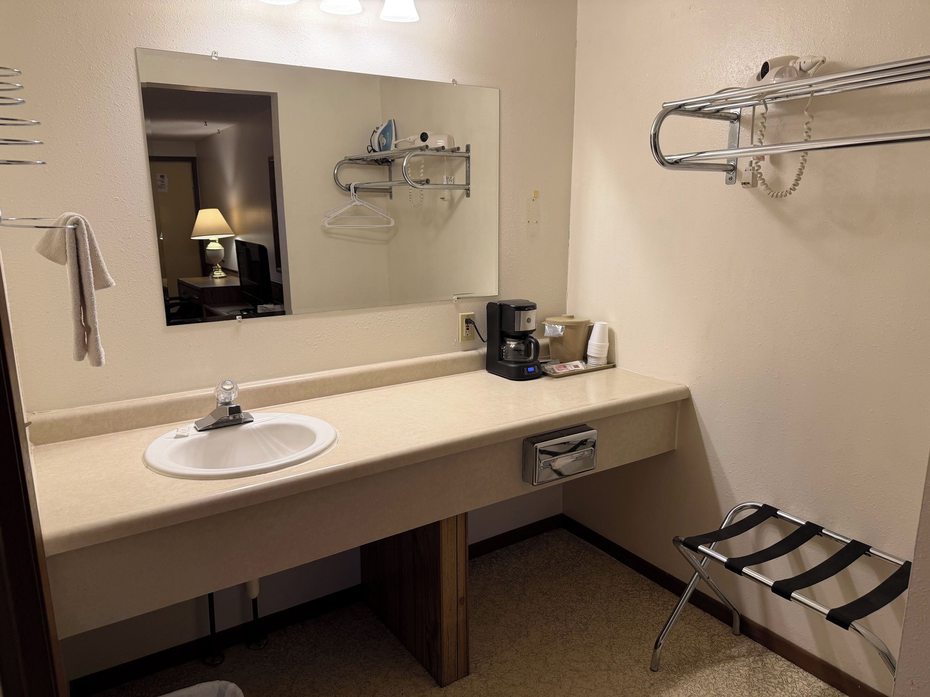 Une salle de bain d’hôtel équipée d’un lavabo, d’un miroir, d’un porte-serviettes et d’une étagère contenant des articles de toilette.