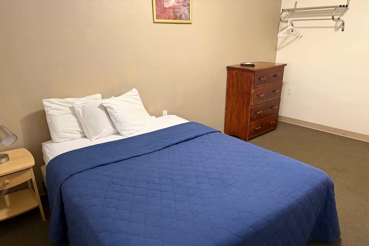 A neatly made bed with a blue quilt, a wooden dresser, and a wall-mounted towel rack.