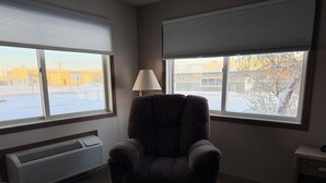 A room with a single armchair, a standing lamp, and a window with blinds. - Sagebrush Inn (Baker)