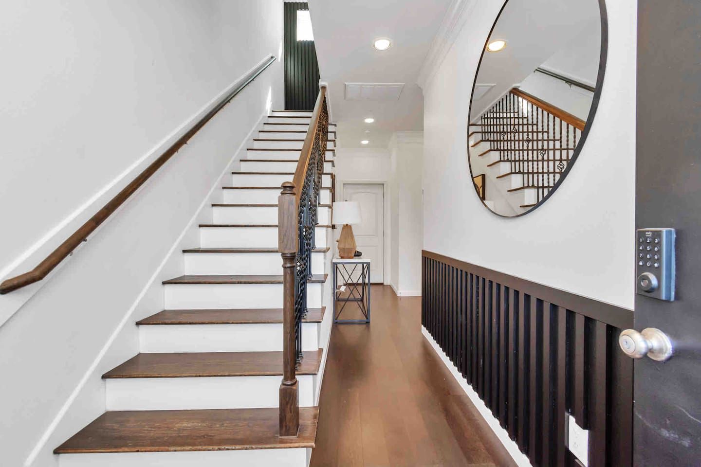 Un escalier avec des marches en bois et une rampe en métal, menant à un palier où se trouvent une porte et une petite table.