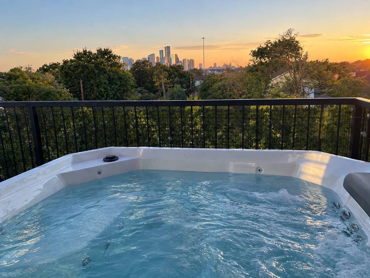 A hot tub with a city skyline view, surrounded by trees and a black railing.