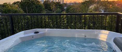 A hot tub with a city skyline view, surrounded by trees and a black railing.