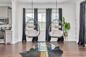 Una sala moderna con dos sillas colgantes, una mesa de centro de vidrio y una cocina al fondo.