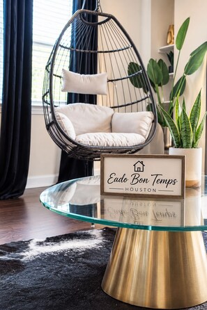 A room with a hanging chair, a glass table, a potted plant, and a sign with 'Eado Bon Temps Houston' written on it. - Eado Bon Temps Serene 4-bedroom house with private rooftop Hot Tub - Minutes ... (Houston)