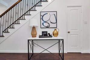 A staircase with black balusters, a white door, a table with a lamp, a vase, and a framed abstract painting. - Fall Discounts -Private Rooftop Hot Tub - Minutes to Downtown- Skyline Views (Houston)
