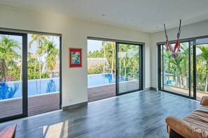 A spacious room with large sliding glass doors leading to a pool area, a framed picture on the wall, and a hammock hanging by the window.
