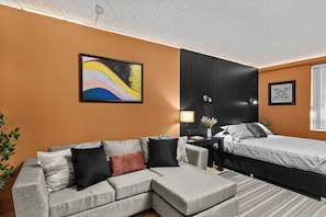 Een moderne hotelkamer met een modulaire bank, een enkel bed, een zwarte accentmuur en een ingelijst abstract schilderij.