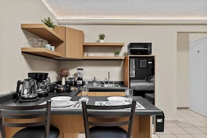 Een kleine keuken met een eettafel, stoelen en moderne apparatuur.