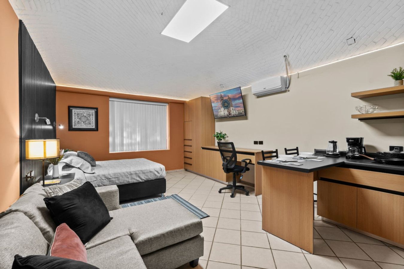 A compact living space with a kitchenette, a sofa, a desk, and a chair.