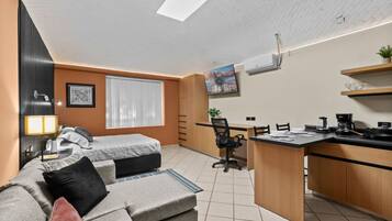 A compact living space with a kitchenette, a sofa, a desk, and a chair.