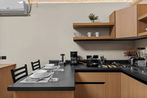 A modern kitchen with a black countertop, wooden cabinets, a coffee maker, and a small plant on a shelf. - Centro Histórico | Cochera | Mini split | Wifi (Durango)