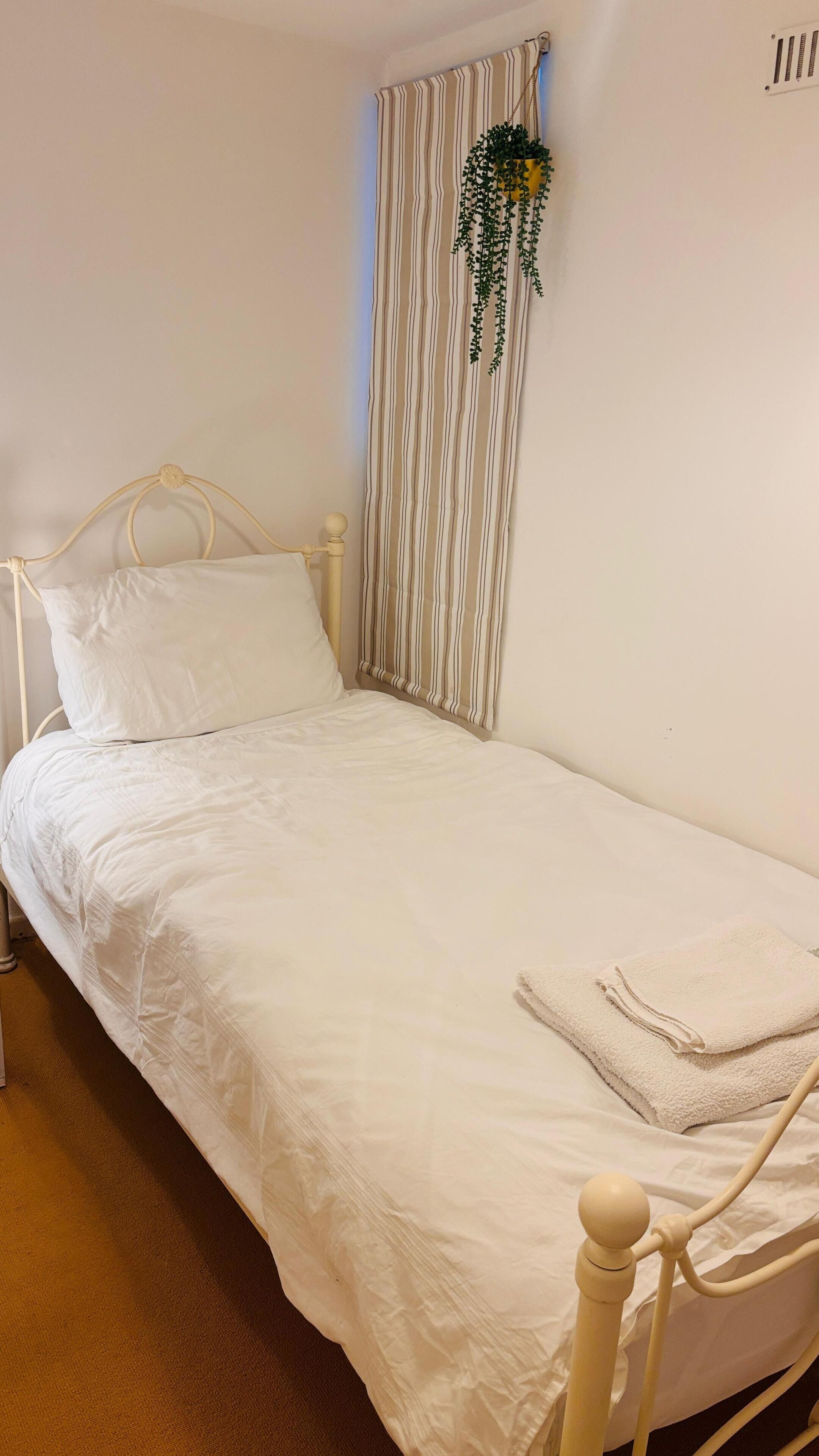 Ein Einzelbett mit weißer Bettwäsche, einem Kopfteil und einer kleinen Topfpflanze an der Wand.