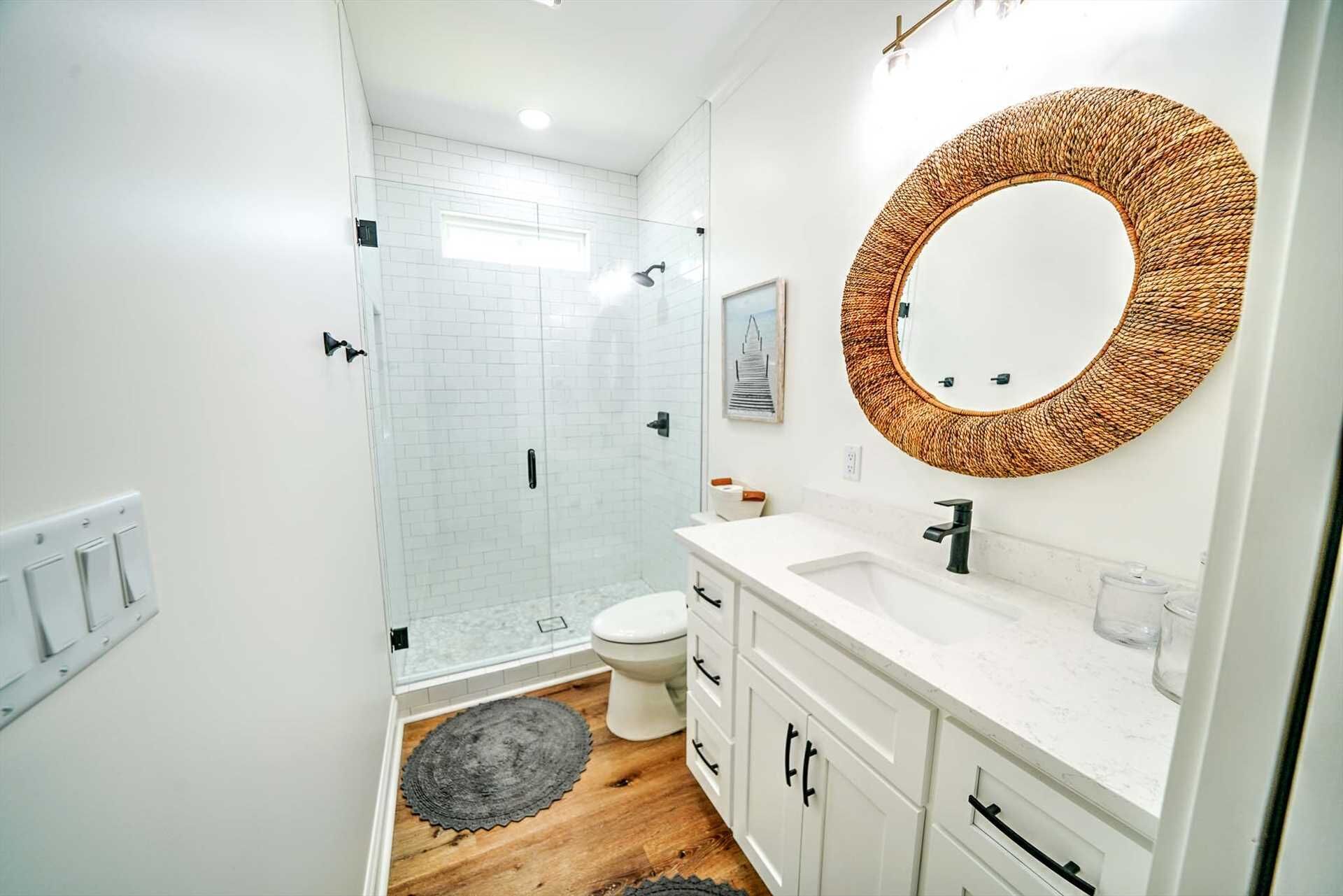 A modern bathroom with a glass shower enclosure, a white toilet, and a vanity with a woven mirror.