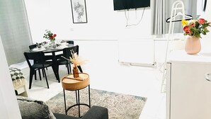 A modern living room with a dining area, a small round wooden table, black chairs, a white cabinet, and a TV mounted on the wall. - One Bedroom Flat D Kentish Town (London)