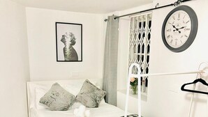 A modern bedroom with a bed, a bedside table, a hanging light, a clock, and a framed picture on the wall. - One Bedroom Flat D Kentish Town (London)