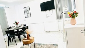 A modern kitchen with a white refrigerator, a dining area with a table and chairs, and a TV mounted on the wall. - One Bedroom Flat D Kentish Town (London)