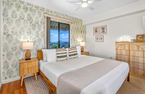 A bedroom with a bed, nightstands, a wooden dresser, and a window with a view. - Pacific Shores B-409 - Beautifully Renovated Ocean View, 2 BD / 2 BA, Split AC! (Kihei)