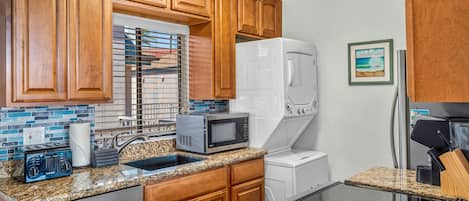 A kitchen with wooden cabinets, a microwave, a refrigerator, a dishwasher, and a glass-top island.