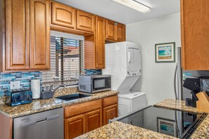 A kitchen with wooden cabinets, a microwave, a refrigerator, a dishwasher, and a glass-top island. - Pacific Shores B-409 - Beautifully Renovated Ocean View, 2 BD / 2 BA, Split AC! (Kihei)
