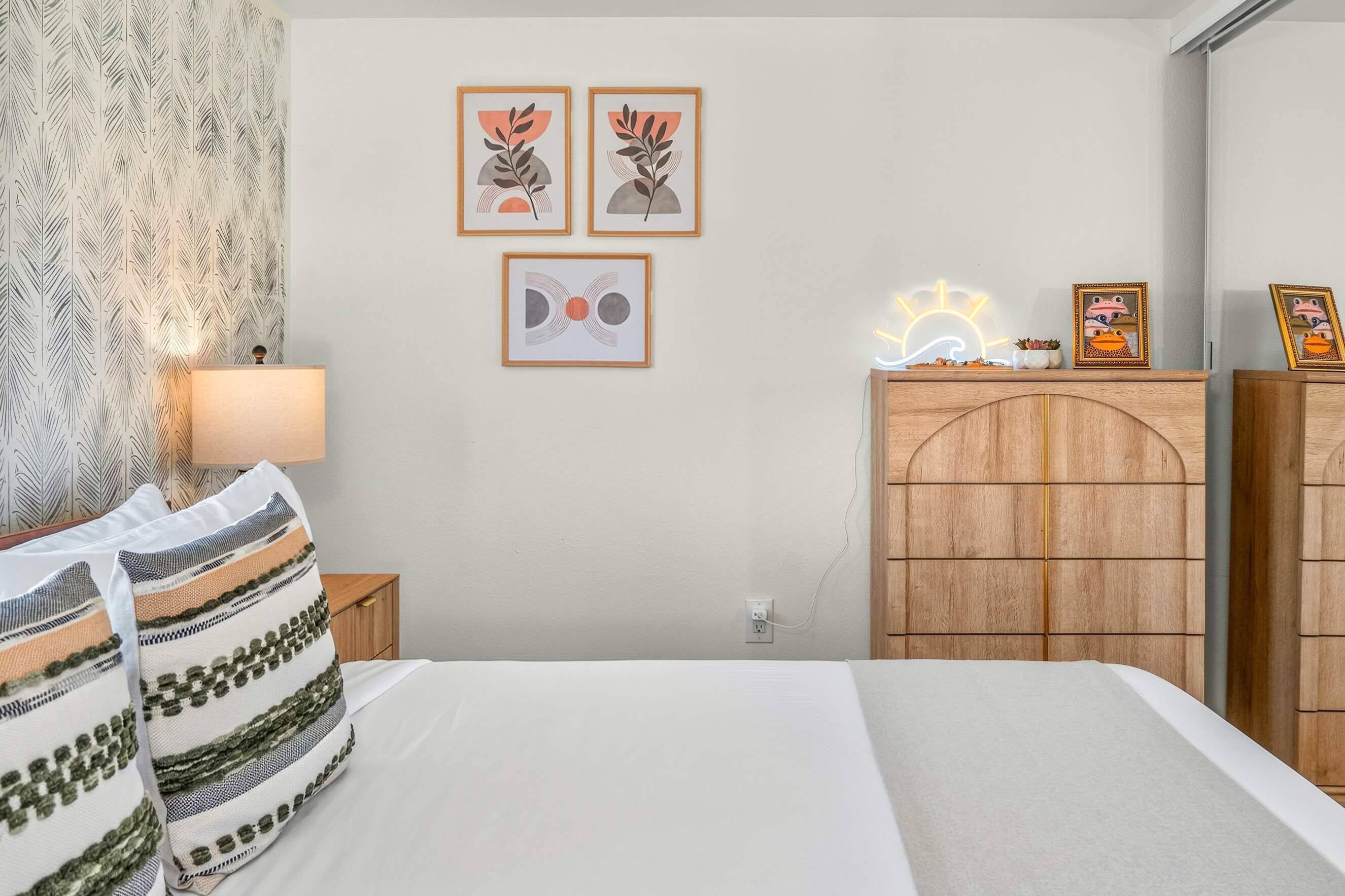 A bedroom with a bed, a nightstand, a lamp, a dresser, and wall art.