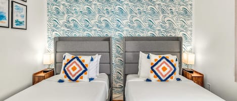 A hotel room with two beds, a patterned headboard, and a nightstand with a lamp.