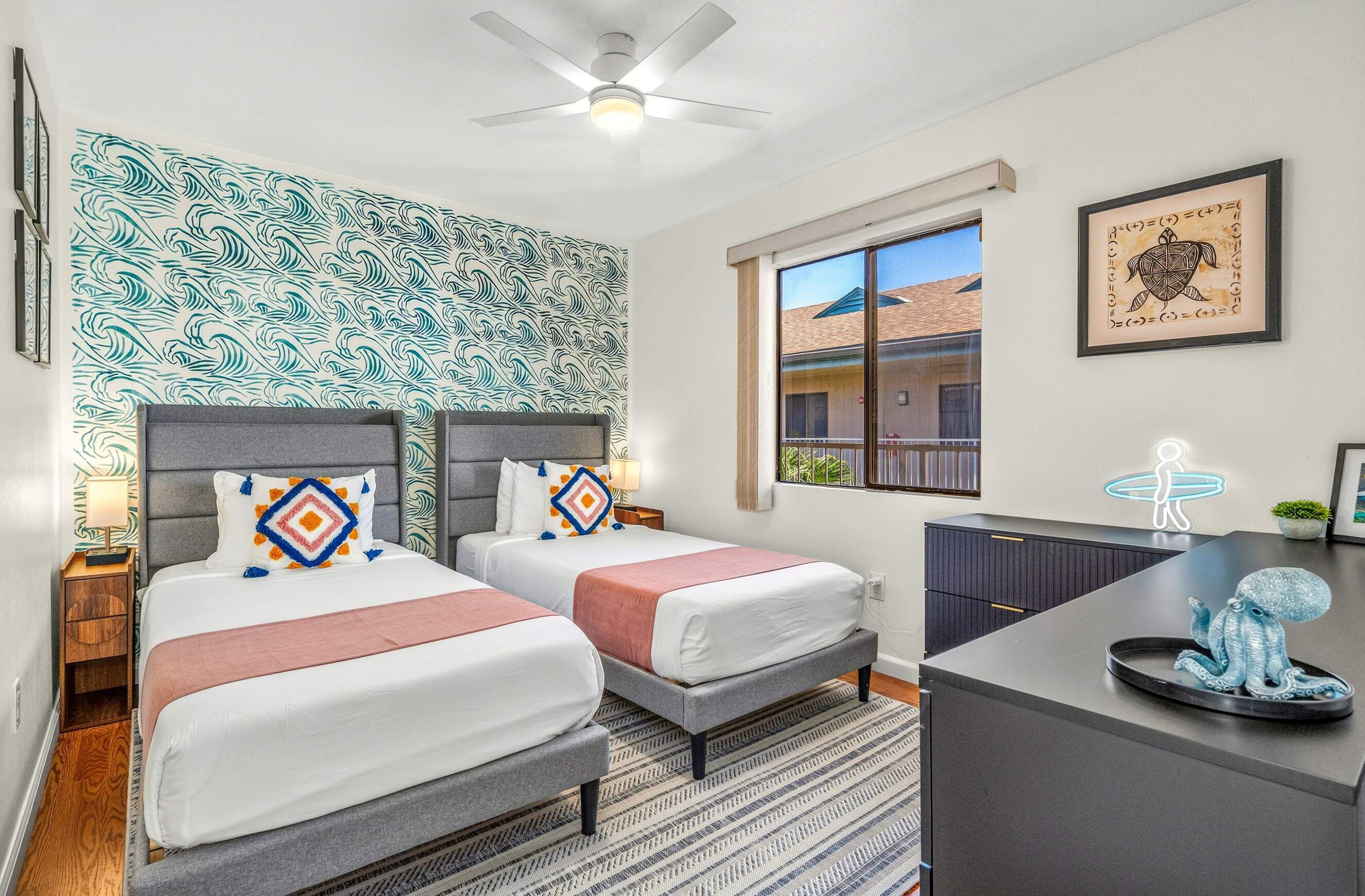 A hotel room with two beds, a desk, a ceiling fan, a window with a view, and a wall with a wave pattern.