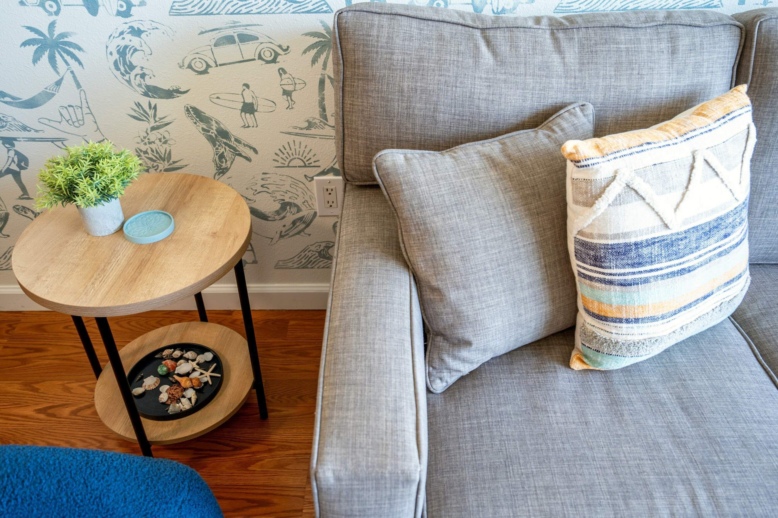 A grey sofa with a striped pillow and a small round table with a plant and decorative items.