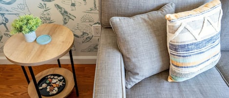 A grey sofa with a striped pillow and a small round table with a plant and decorative items.