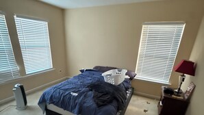 A bedroom with a bed, two windows with blinds, a heater, a nightstand with a lamp, and a carpeted floor. - Spacious 4-bedroom house in fantastic Marietta with AC (Marietta)