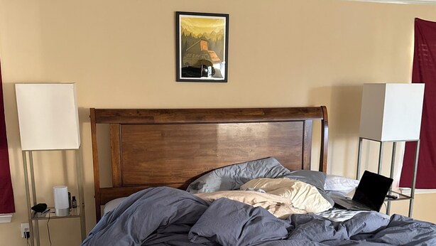 A bedroom with a wooden bed, a nightstand, a lamp, and a painting on the wall. - Spacious 4-bedroom house in fantastic Marietta with AC (Marietta)