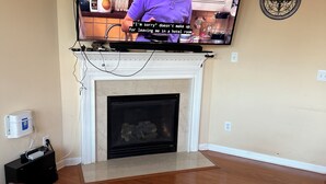 A hotel room with a television mounted above a fireplace, a wooden floor, and a small table with a children's toy and a magazine. - Spacious 4-bedroom house in fantastic Marietta with AC (Marietta)