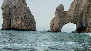 Paesaggio costiero con due formazioni rocciose che creano un arco naturale sul mare.