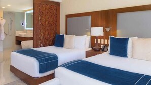 Una camera d'albergo con due letti, una testiera in legno, un comodino con una lampada e un bagno visibile sullo sfondo.