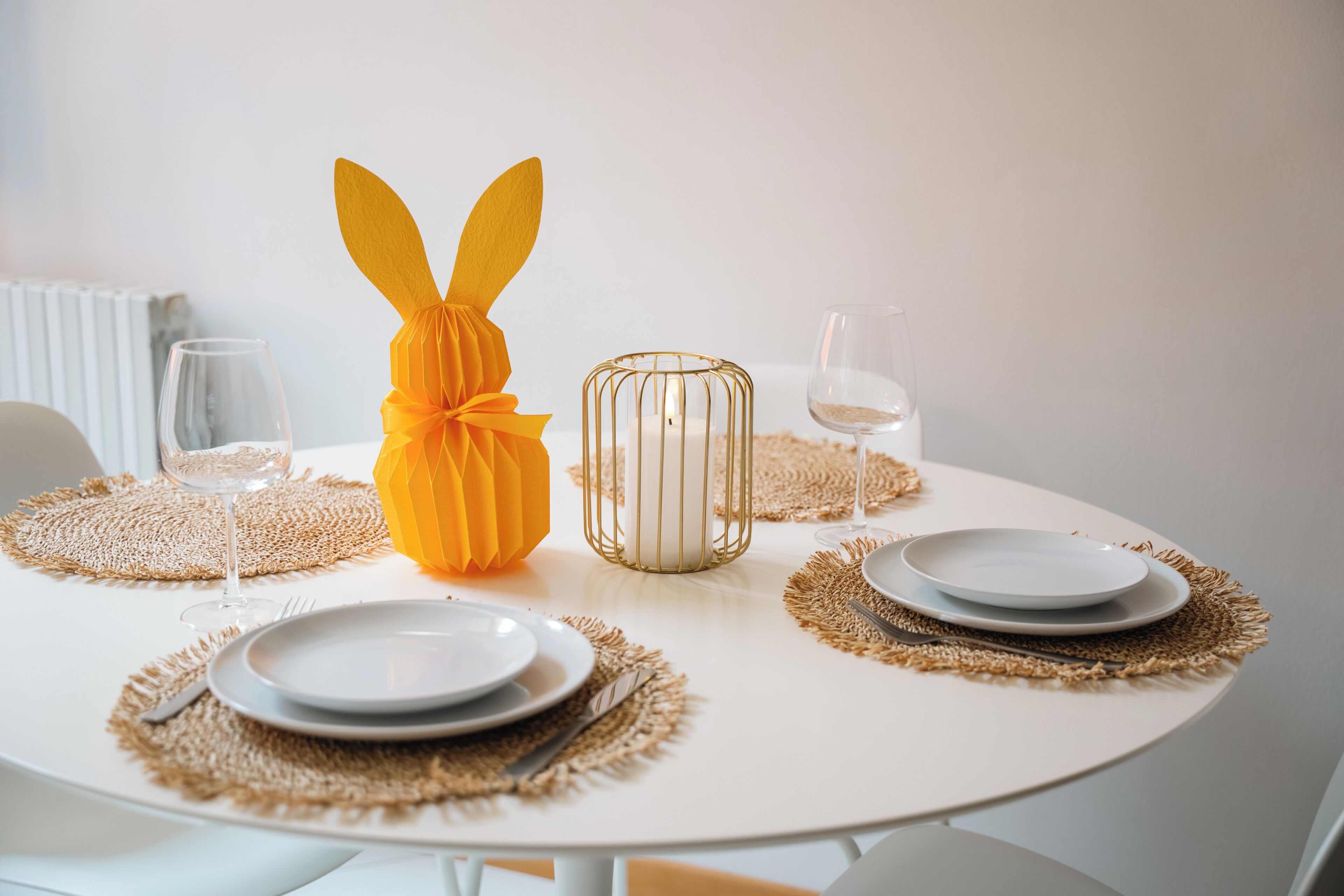A round dining table with white plates, gold wire candle holder, and a decorative orange bunny centerpiece.