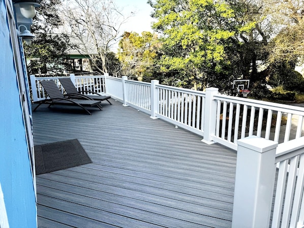 A wooden deck with white railings, two lounge chairs, and a basketball hoop. - Oceanside, GOLF CART, 3BR/2BA Home, Premier Location (Emerald Isle)