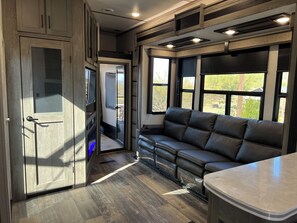 A modern RV interior with a leather sofa, a dining area, and a kitchen.