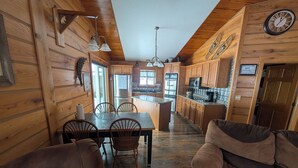 A cozy cabin-style kitchen with wooden walls, a dining area with chairs, and a central island. - Golf, Relax, Repeat – Cabin Close to the Golf Course & Downtown EVL (Great Valley)
