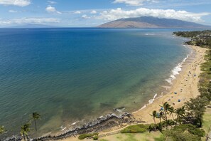 A beach with clear waters, a sandy shore, and a mountain in the background. - Kamaole Beach Royale 506 - Stunning Ocean Views, Spectacular Renovation, AC (Kihei)
