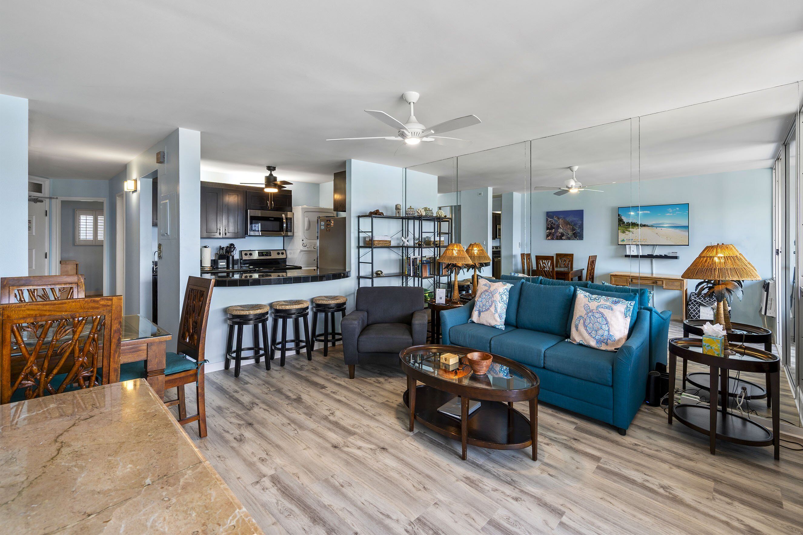A spacious living area with a blue sofa, wooden dining table, and kitchen in the background.