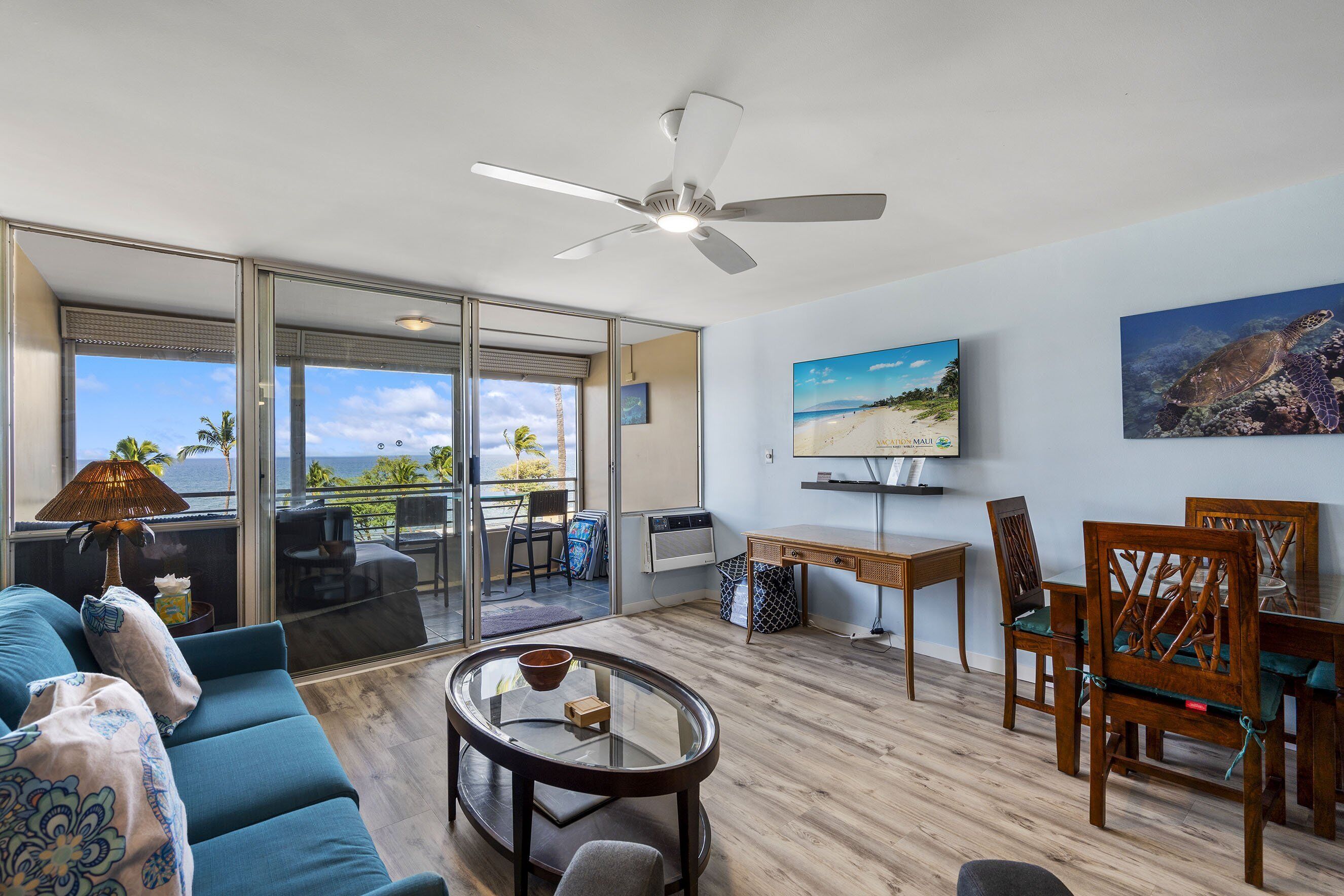 Ein modernes Wohnzimmer mit Glastür zum Balkon, Deckenventilator, Flachbildfernseher und Essbereich mit Holzmöbeln.