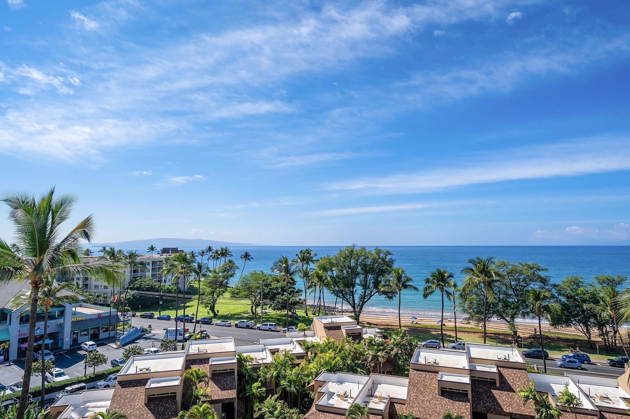 A coastal hotel with multiple buildings, a parking lot, and a view of the ocean.