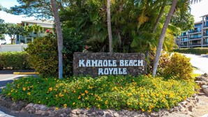 Une enseigne pour le Kamale Beach Royale, avec une bordure en pierre et des fleurs jaunes devant.