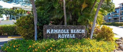 Une enseigne pour le Kamale Beach Royale, avec une bordure en pierre et des fleurs jaunes devant.