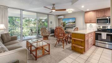 A spacious living area with a sofa, coffee table, and wicker chairs, a dining area with a table and chairs, and a kitchen with modern appliances and wooden cabinets.
