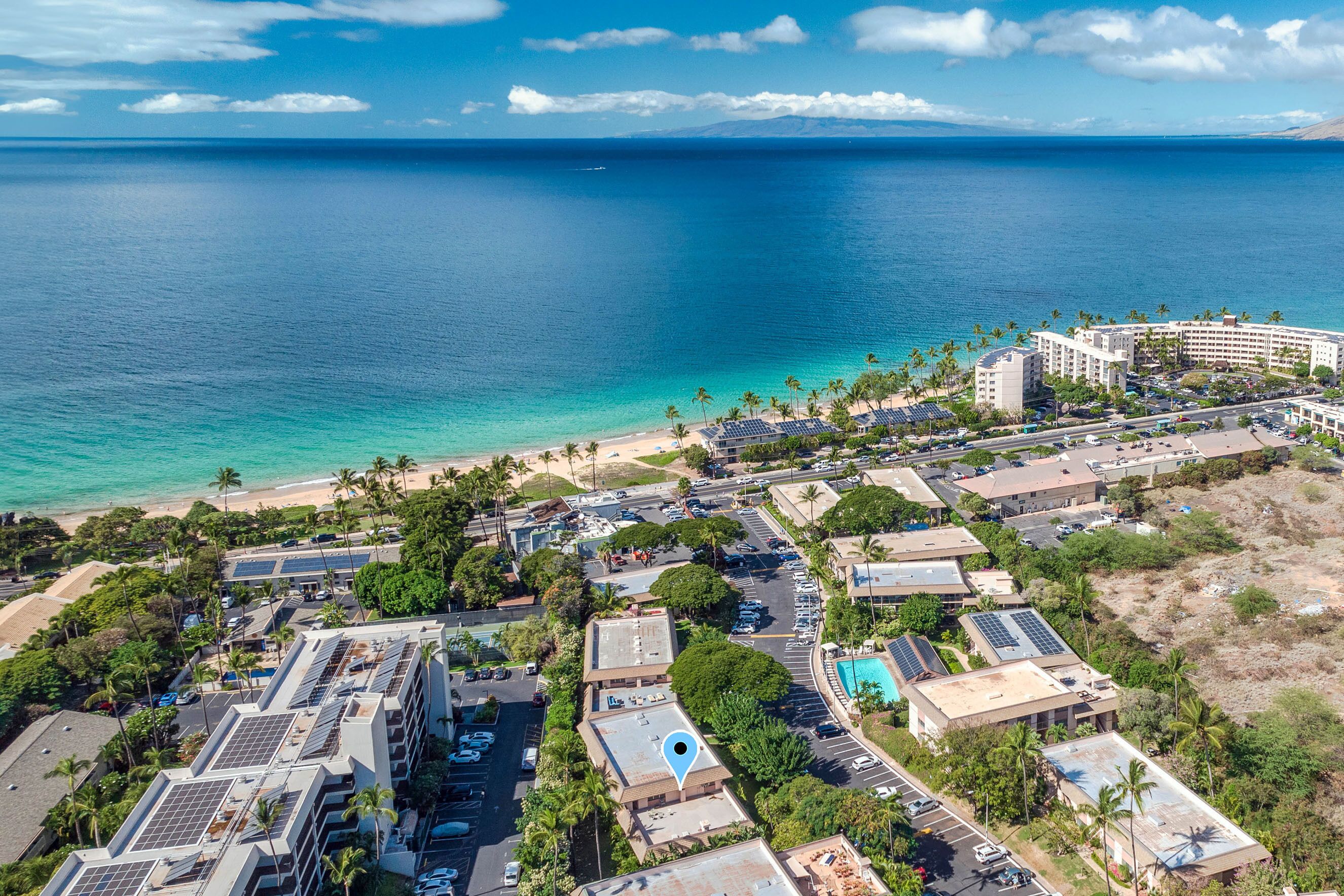 An aerial view of a coastal resort area with buildings, a beach, and a clear view of the ocean.