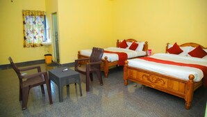Ett hotellrum med två sängar i trä, var och en med röda kuddar, ett litet bord, två stolar och ett fönster med en blommig gardin.