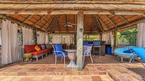 An outdoor patio area with a thatched roof, wicker furniture, and a tiled floor. - Charming Alamo Heights Studio (San Antonio)