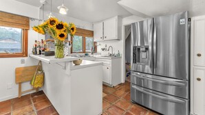 A modern kitchen with white cabinets, a stainless steel refrigerator, and a central island with a vase of sunflowers. - Charming Alamo Heights Studio (San Antonio)