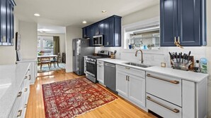 Una cucina moderna con mobili blu scuro, ripiani bianchi e un tappeto rosso con motivi.